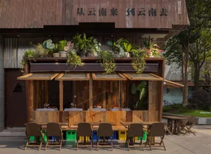 Outdoor seating area of a wooden street cafe with green plants and tables.