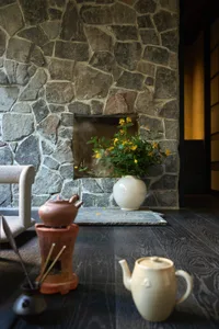 A cozy living room with a stone fireplace, wooden floor, and a white vase with yellow flowers.
