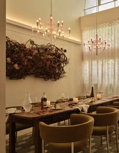 Industrial-style restaurant interior with wooden table, fabric chairs, glass vases, and metal accents.
