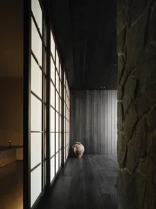 A minimalist modern interior space featuring wood paneling and traditional Japanese shoji screens, with a vase on the floor.