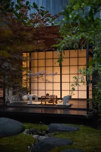 A serene Japanese tea terrace with seating and a table, surrounded by stone and greenery.