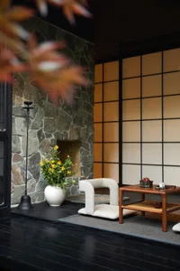 A modern living room with stone walls, a wooden table, a white vase with yellow flowers, and a cozy chair.