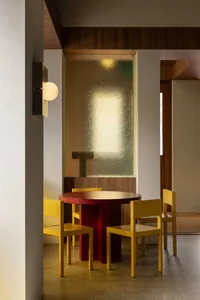Modern restaurant interior featuring a wooden round table surrounded by yellow chairs.