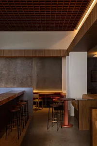 Modern restaurant interior featuring wooden tables, concrete walls, and leather seating.