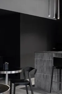 A modern cafe bar interior with black chairs, a grey high counter, and concrete walls.