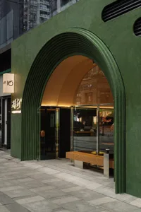 A modern storefront with a green concrete structure and a wooden bench inside.