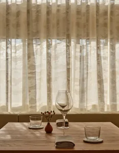 A minimalist restaurant table setting with natural fiber curtains in the background.