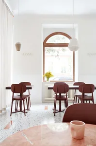 A minimalist cafe interior with terrazzo flooring, white walls, and wooden chairs.