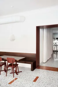 A minimalist dining room with a wooden table, terrazzo floor, and white pendant light.