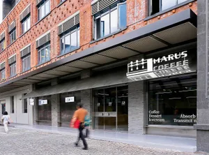 A modern coffee shop with a brick exterior, glass storefront, and metal awning on a cobblestone street