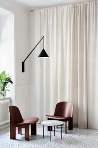 A modern lounge featuring fabric curtains, a metallic lamp shade, marble table, and resin floor.