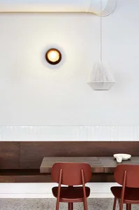 A minimalist cafeteria with wooden furniture and white walls, featuring hanging lights and a built-in bench and table.