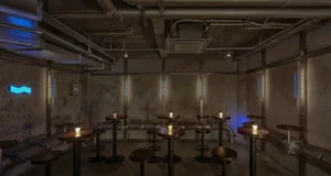 Industrial-style bar room with metallic tables and stools, blue neon lights, and exposed concrete walls and ceiling.