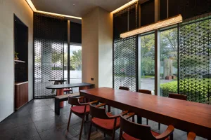 Modern restaurant interior with wooden tables, red cushioned chairs, and glass partitions.