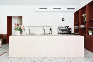 A modern minimalist coffee shop bar with concrete countertops, wooden shelves, and metal coffee machines, featuring a sleek a