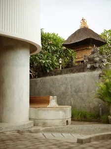 Concrete seating area with wooden bench in a garden setting, featuring a traditional Balinese pavilion with thatched roof in 
