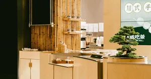 A wooden restaurant interior with a bamboo backdrop and bonsai tree.