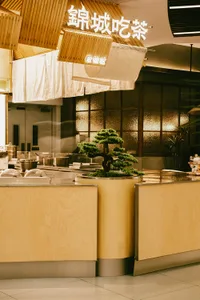A modern restaurant featuring wooden tables, glass panels, and a bonsai tree centerpiece.