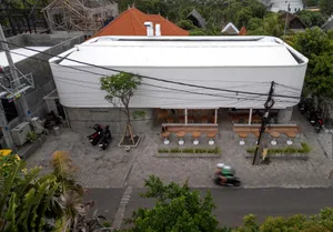 A modern urban cafe with a white metal and concrete exterior, featuring outdoor seating and a sleek design.