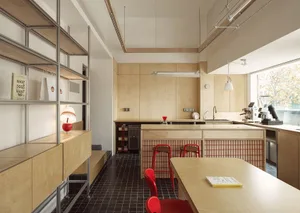 An interior view of a cafe featuring wood plywood walls and counters, red stools, and a black and white tiled floor.