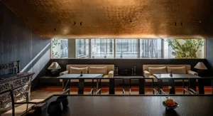 Modern industrial-style restaurant interior with metallic ceiling tiles, minimalist furniture, and large windows.