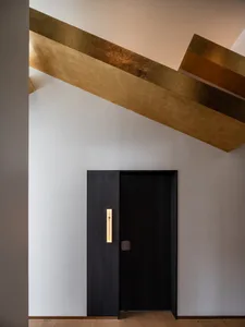 A minimalist interior design featuring a black door with gold trim and a metal ceiling.