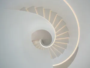 Modern, minimalist white concrete spiral staircase with illuminated edges.