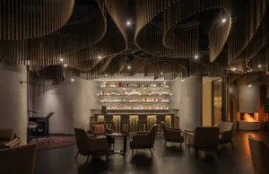 A modern bar and lounge interior with dark accents, featuring a wooden ceiling design and metal railings.