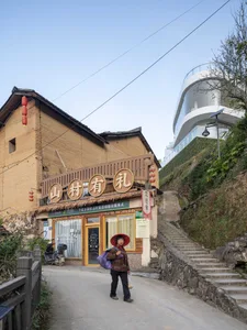 An old brick building sitting on a hillside street with a woman standing in front.