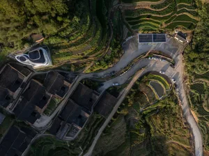 Aerial view of a terraced hillside village with winding roads and solar panels.