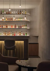 A stylish bar interior featuring concrete shelves filled with bottles of alcohol, set against a modern design backdrop with m