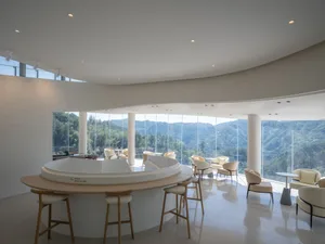 Modern cafe interior with glass walls and wooden furniture, overlooking scenic mountains.