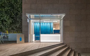 Modern, sleek glass entrance to a coffee shop with blue accents and white counter.