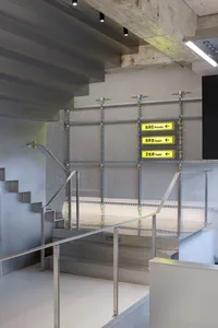 An industrial minimalist office space with metal stairs, concrete walls, and glass railings.