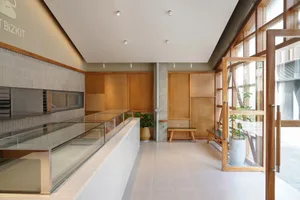 A minimalist retail space featuring glass doors, wooden benches, and concrete flooring.
