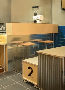 Modern wooden coffee shop bar counter with stools and espresso grinder.