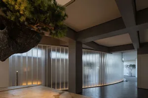 Modern hotel lobby featuring concrete walls and curved glass wall with illuminated lighting.
