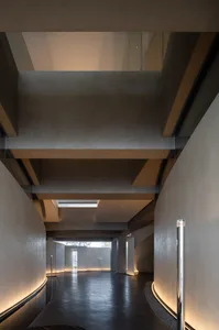 A modern lobby interior with concrete walls and floor, illuminated by warm lighting.