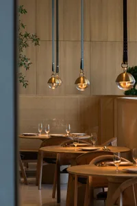 Modern restaurant dining room with wooden tables, chairs, and pendant lights.