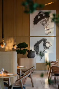 A modern restaurant interior with wooden walls, hanging lamps, and abstract paintings.