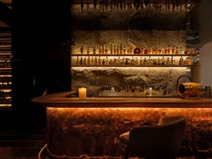 A well-lit stone and wooden bar interior with various bottles of alcohol lined up on shelves.