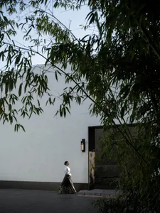A woman wearing a black dress is walking towards a white wall with a black framed glass door.