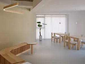 Modern cafe space featuring wooden furniture, light fixtures, and natural light through large windows.