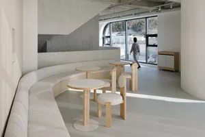 A minimalist restaurant seating area with white fabric seating and wooden tables.