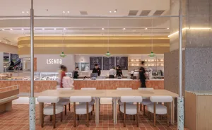 A modern cafe with minimalist design elements featuring a terrazzo floor and white cushions on chairs.
