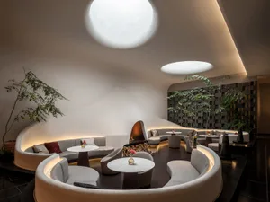 An elegant, modern hotel lobby with curved seating areas, a fireplace, and natural light from skylights.