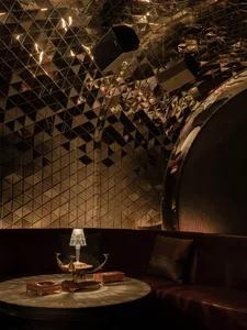 A modern restaurant interior featuring metallic walls and a round, metallic table with a lamp.