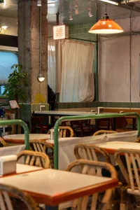 A rustic restaurant interior with wooden tables, metal railings, and green plants.