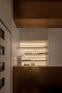 A modern bar area with glass shelves containing various glassware and drinks, illuminated by soft lighting.