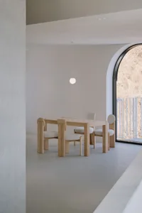 A modern interior space featuring four-legged wooden furniture with cushioned seats and a checkered wooden table.